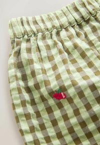 Rohelise ja pruuni ruudulise mustriga kangas elastse vöökohaga, millel on külje peal väike tikitud punane kirsi detail. Pehme tekstuur.