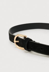 Sort ruskindsbælte med spænde i guldmetal og en glat finish, med en smal rem og justerbare huller for pasform.