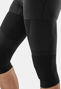 Schwarze Sportleggings mit einer Mischung aus Texturen, die glatte und gerippte Bereiche aufweisen, eine enganliegende Passform haben und knielang geschnitten sind.