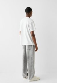 Vit kortärmad t-shirt i kombination med löst sittande, ljusgrå jeans. Outfiten har diskreta sömmar och kompletteras av off-white sneakers.