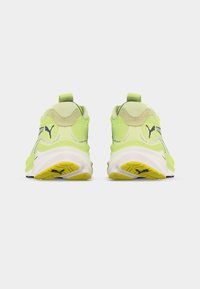 Ζευγάρι ανοιχτόχρωμων πράσινων αθλητικών παπουτσιών Puma, εμφανισμένα από πίσω, με λευκές ενδιάμεσες σόλες και κίτρινες εξωτερικές σόλες σε λευκό φόντο.