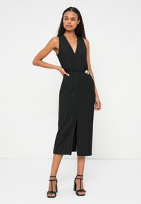 Abito midi a righe nere con scollatura a V profonda, vita aderente e spacco. Presenta una cintura con un accento metallico e design senza maniche.