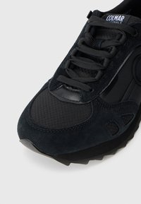 Sneaker de sport noire en mélange de matériaux en suède et en maille, avec des panneaux texturés, un bout rond et des lacets plats.