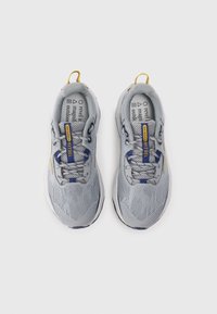 Baskets de sport grises avec une tige en mesh, accents jaunes et bleus, lacets ronds et semelle texturée contrastante. Logo notable sur la languette et la semelle intérieure.