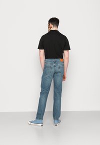 Conjunto de hombre que incluye una camiseta polo negra de manga corta, jeans de mezclilla azules y zapatillas de deporte azul claro. Parche de cuero marrón visible en la cinturilla.