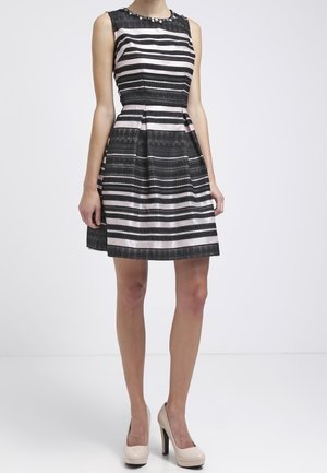 Ärmelloses knielanges Kleid mit schwarzen, weißen und hellrosa horizontalen Streifen, taillierter Passform, kombiniert mit beigen High-Heels.