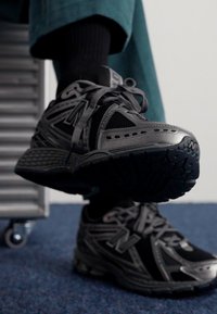 Juodos ir pilkos sportinės bateliai su tinklelio ir gumos medžiagomis, turintys tekstūruotą padas, akį traukiantis raištelių sistema ir modernūs dizaino akcentai.