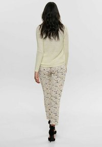 Hellgelbes Strickpullover und gemusterte Hose mit pastellfarbenen Blumen und schwarzen Akzenten, kombiniert mit schwarzen Absätzen, von hinten betrachtet.