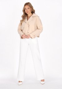 Giacca beige a doppio petto cropped con grandi bottoni, abbinata a pantaloni bianchi a gamba larga. Tessuto morbido con una leggera lucentezza, dettagli minimi.