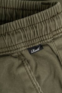 Grüner Stretchstoff mit gerafftem Bund und sichtbaren Nähten. Ein schwarzes Etikett mit weißem Text zeigt die Marke "Reell."