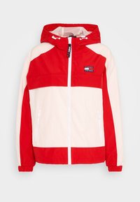 Czerwona i kremowa kurtka przeciwwiatrowa z kapturem, z zamkiem błyskawicznym z przodu, dwoma bocznymi kieszeniami i logo Tommy Jeans na piersi.