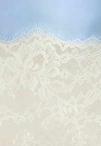 Tissu en dentelle florale blanche délicate avec des bords en forme de festons sur un fond bleu clair, mettant en valeur des détails fins de fil et des motifs complexes.