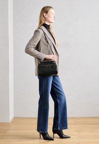 Borsa nera strutturata con tracolla, finitura testurizzata e dettagli in hardware dorato. Abbinata a un blazer a scacchi e jeans a gamba larga.