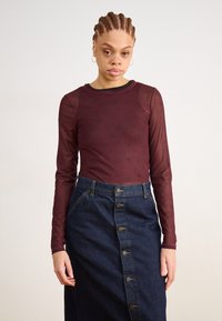 Μακρυμάνικη μπορντό μπλούζα με διακριτό σχέδιο, συνδυασμένη με σκούρα τζιν φούστα με μπροστινά κουμπιά και πλαϊνές τσέπες.