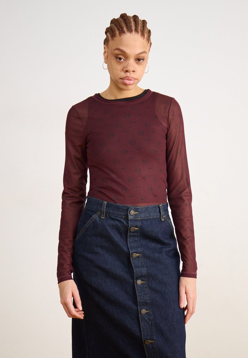 Langermige bordeaux top met een subtiel patroon, gecombineerd met een donkere denim rok met knopen aan de voorkant en zijzakken.