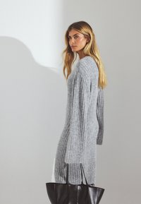 Hallide ribatekstiiliga kampsunkleit pikade varrukatega, pehme tekstuuriga, koos musta õlakotiga. Minimalistlik disain, külgvaade.