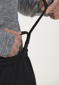 Sorte atletiske bukser har en elastisk talje med justerbar snor. Bæreren holder i snoren, som har et struktureret greb.