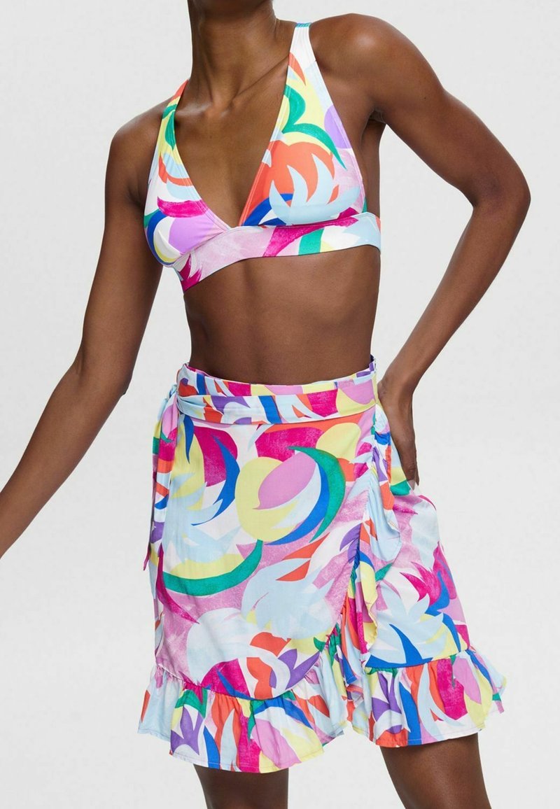 Femme portant un haut de bikini à imprimé abstrait multicolore et une jupe portefeuille taille haute assortie avec un ourlet volanté.