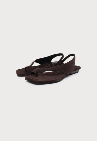 Sandales plates en daim marron foncé avec boucle pour l’orteil et bride arrière sur fond blanc.