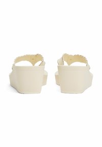 Sandalias de cuña con una suela suave de color beige claro y correas texturizadas. Presentan un diseño con bordes scallop en las correas y un respaldo seguro.