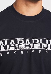 Mörkblå bomullströja med rund hals, med en stor vit sliten "NAPAPIJRI"-logotyp över bröstet och en strukturerad yta.