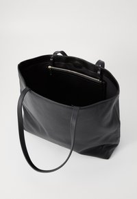 Zwarte leren tote bag met een gladde textuur, open bovenkant, lange handvatten en een ritsvak aan de binnenkant voor organisatie.