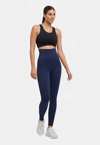 Zwarte sportbeha en marineblauwe, getextureerde legging met aansluitend ontwerp en hoge tailleband, gecombineerd met witte sportschoenen.