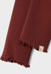 Bordeauxfarbener Stoff mit weicher Textur und fransigen Kanten. Ein kleines Etikett ist sichtbar, auf dem der Markenname „Lil Atelier“ steht.