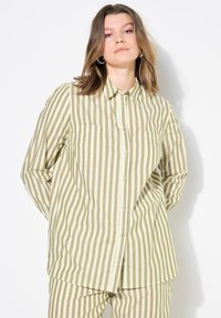 Camisa de botones a rayas en verde oliva y blanco roto, con cuello, dos bolsillos en el pecho y un corte relajado. Tejido ligero y mangas largas.
