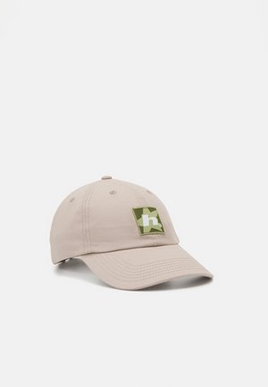 Beige cotton baseball cap with a curved brim, featuring a green and white logo patch on the front. Soft texture, structured design.