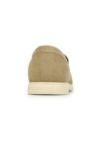 Zapatos de ante en marrón claro con una textura suave. Presentan una forma redondeada y una suela de goma beige. Costura simple a lo largo de la parte trasera.