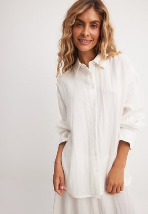 Witte, oversized button-up blouse gemaakt van een lichte, gestructureerde stof. Heeft een puntige kraag en ontspannen mouwen.