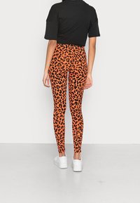 Orange leopardmönstrade leggings i stretchigt material med en åtsittande design. Matchas med en svart kort topp och vita sneakers.