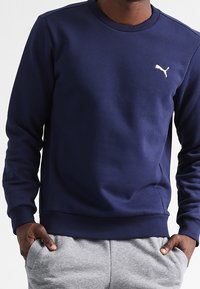 Námořnická modrá mikina vyrobená z jerseyské látky, s kulatým výstřihem, ribovanými manžetami a malým bílým logem na levé hrudi.