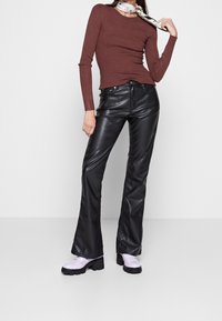 Brązowa prążkowana bluzka z długim rękawem zestawiona z czarnymi, imitującymi skórę, spodniami w stylu dzwonów oraz jasnofioletowymi butami na platformie. Akcent w postaci szalika w kwiatowy wzór.