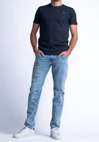 Camiseta de algodón azul marino con mangas cortas, combinada con vaqueros azul claro y zapatillas blancas. El conjunto presenta un diseño sencillo y moderno.