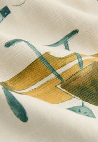 Tkanina bawełniana o kremowym tle, zdobiona abstrakcyjnymi niebieskimi i musztardowożółtymi kształtami, gładka w dotyku, z subtelnymi niuansami kolorystycznymi.