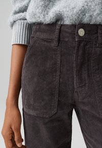 Dark gray corduroy pants feature a front pocket and a button closure at the waistband; paired with a light gray fuzzy sweater.