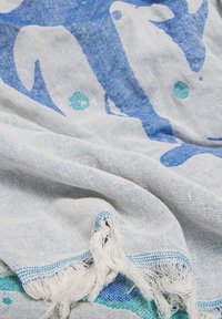 Lightweight cotton scarf featuring a blue and white whale pattern, with green accents. Edges are fringed with a textured weave.