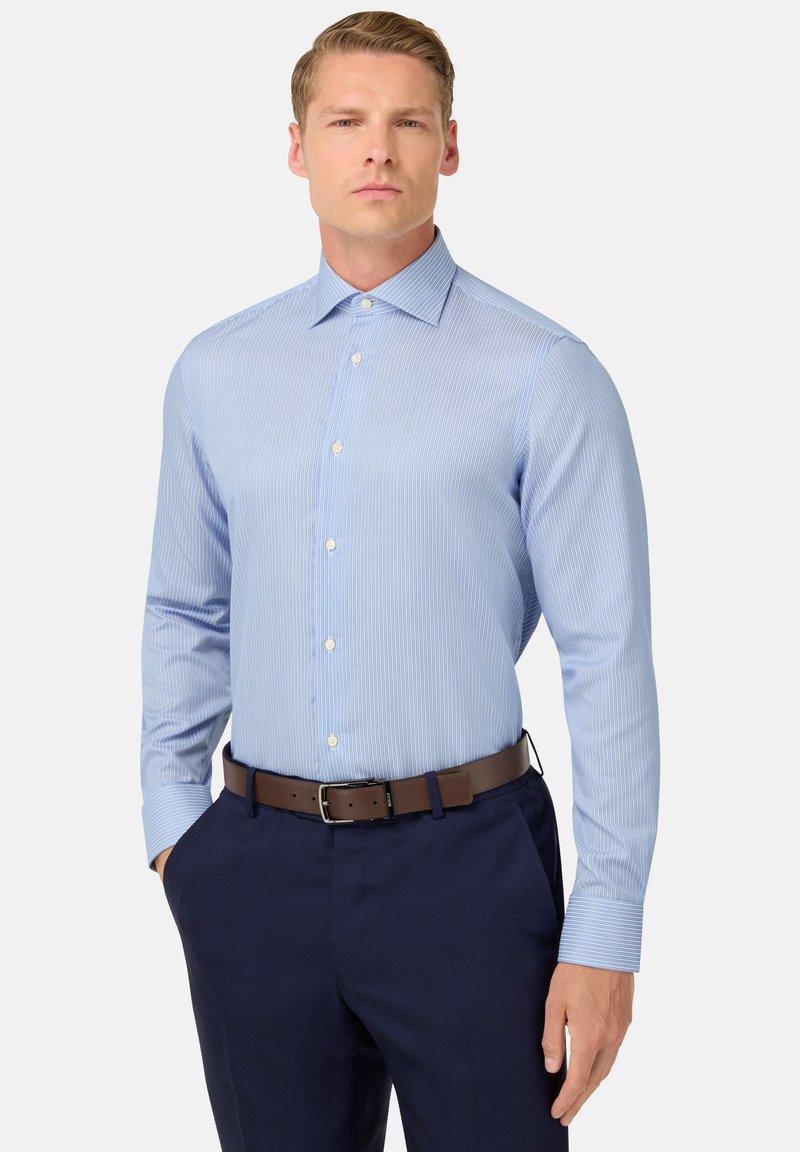 Gaiši zils svītrains krekliņš ar pogu leju, garām piedurknēm un gludu tekstūru, kombinēts ar tumšām biksēm un brūnu jostu.