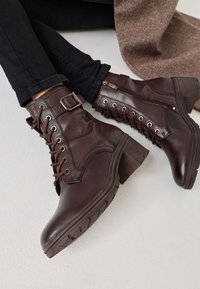 Les bottines en cuir marron présentent une finition texturée, des lacets à l'avant, une fermeture éclair latérale et un talon épais avec une semelle à motif.