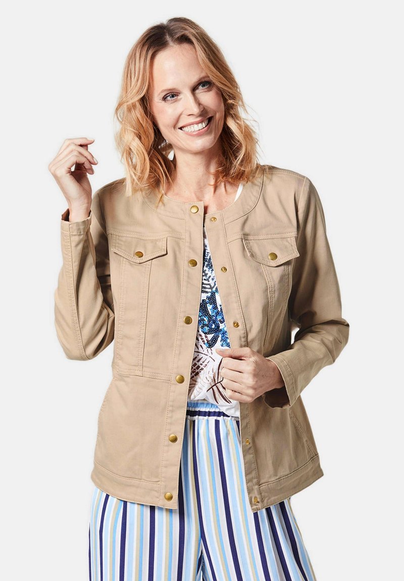 Beige jack met lange mouwen, drukknopen, twee borstzakken en een gladde textuur. Gecombineerd met gestreepte broek.