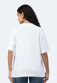T-shirt bianco in cotone, maniche corte, vestibilità rilassata, scollatura rotonda, texture liscia, design semplice, indossato con jeans blu.