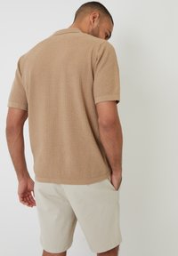 Polo beige de manga corta con patrón texturizado, con cuello y puños acanalados, combinado con pantalones cortos de color claro.