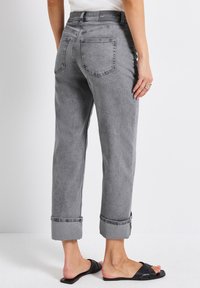 Graue Jeans mit geradem Bein, hochgekrempelten Säumen und zwei Gesäßtaschen. Sie verfügen über eine strukturierte Oberfläche und einen mittelhohen Bund.