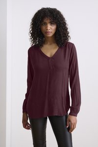 Bordeauxfarbige Bluse mit langen Ärmeln, V-Ausschnitt und Knopfdetails, aus strukturiertem Stoff, kombiniert mit schwarzen Slim-Fit-Hosen.