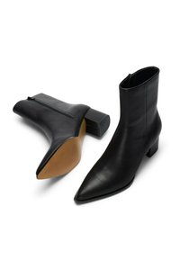 Botines de cuero negro con punta picuda, cierre de cremallera y tacón cuadrado bajo; textura lisa y diseño minimalista.