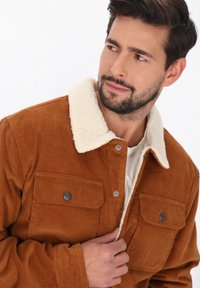 Brun kordfløjlsjakke med en cremefarvet faux shearling krave, trykknapper og to frontlommer med klap.