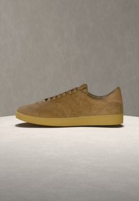 Baskets basses en daim marron avec semelle en caoutchouc couleur tan, design à lacets et détails de coutures subtiles, présentées sur une surface neutre.