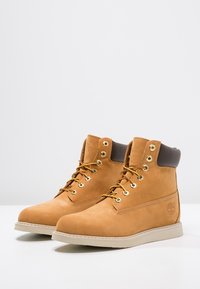 Botas de tobillo de cuero marrón con herrajes dorados, suela beige y parte superior texturizada. Presentan un cuello acolchado y un detalle con el logo en el lateral.